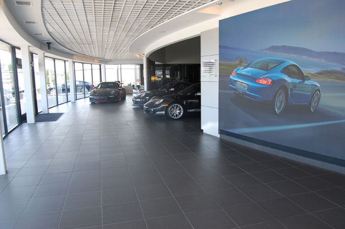 Showroom at Boardwalk Porsche: a large-format dark tile floor under a car, with a wall mural behind